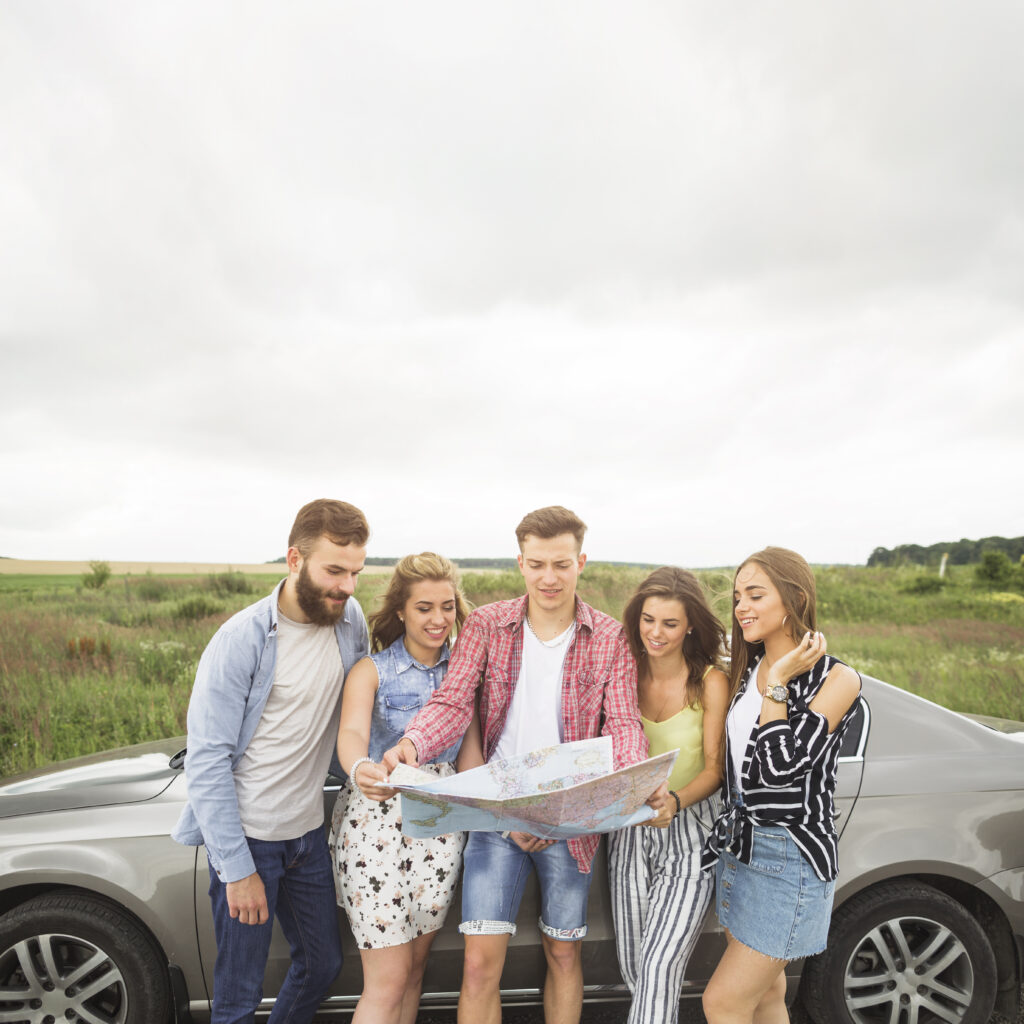 happy-friends-standing-by-car-searching-map